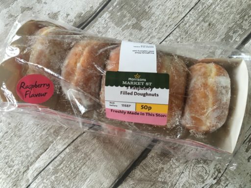 image of five icing sugar-dusted raspberry jam doughnuts in a box. 