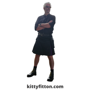 man wearing black kilt and black shirt with doc marten boots stood with folded arms looking off camera.