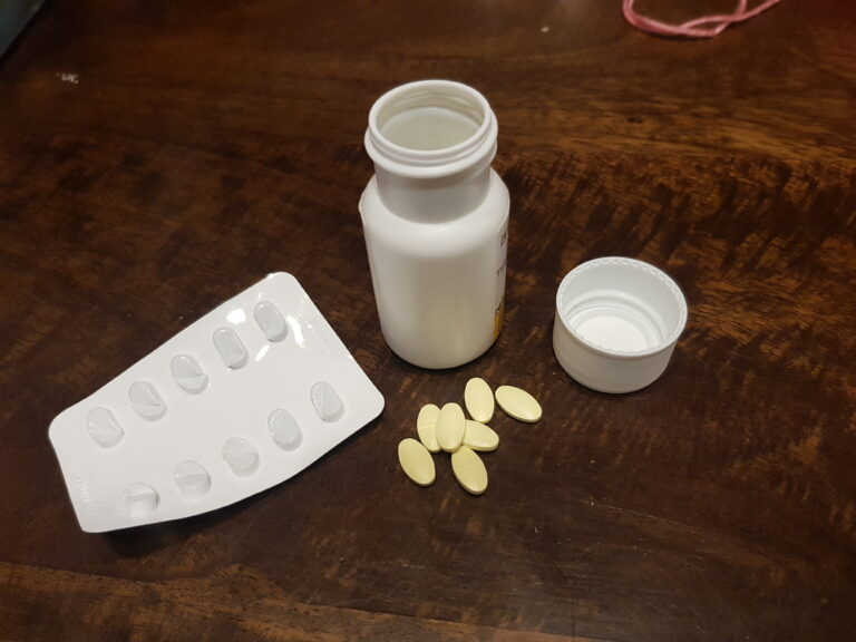 shows pill bottle and a pill blister pack with scattered yellow oval tablets.
